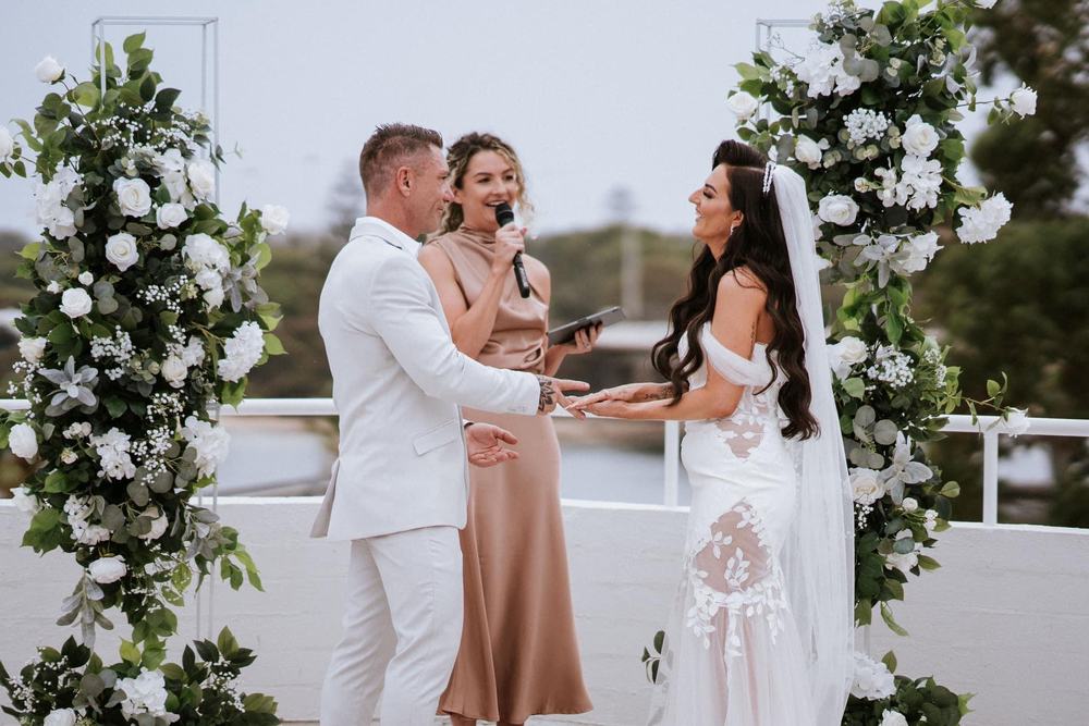 A couple during the ceremony between two tall columns of white flowers