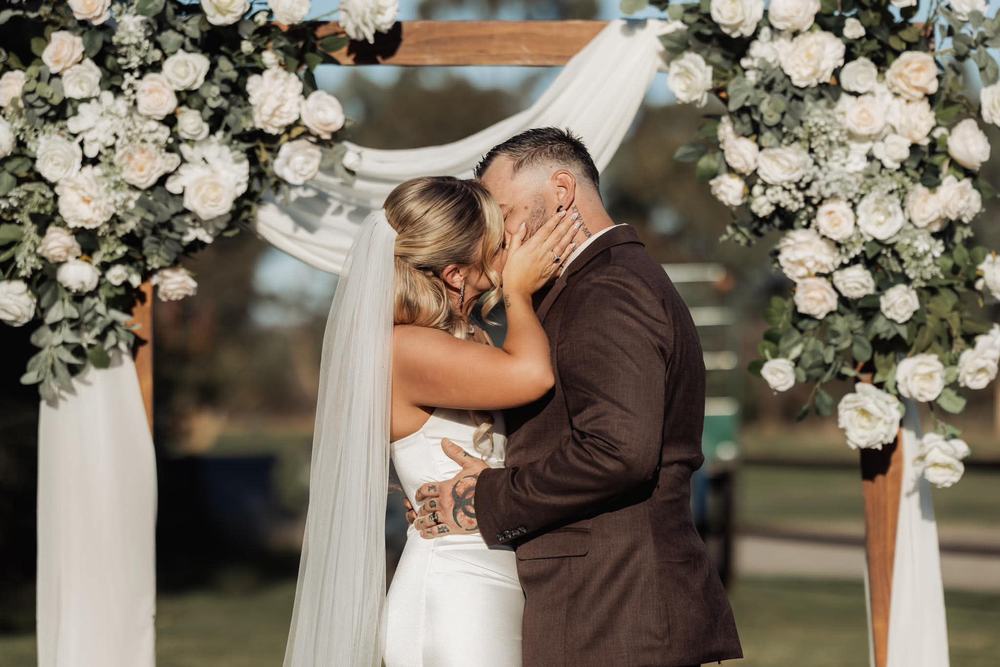 A couple kissing in front of white flowers and draped fabric