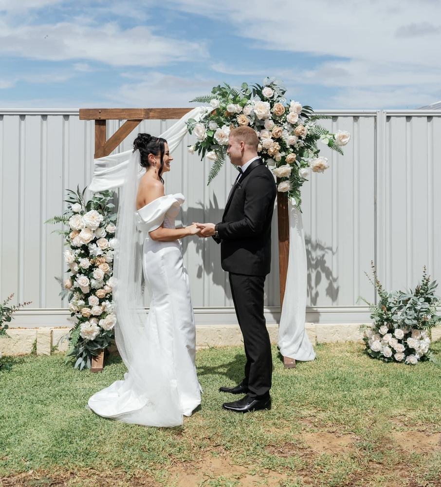 A couple at an outdoor arch with pink and white flowers