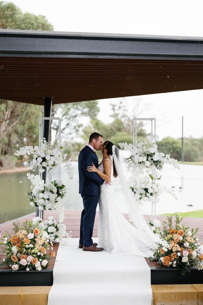 A couple under a pergola with flower stands and a white aisle