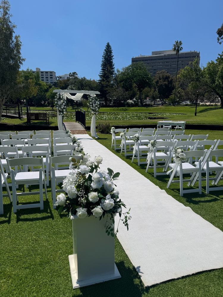 A white pedestal of white flowers beside a white aisle on a lawn