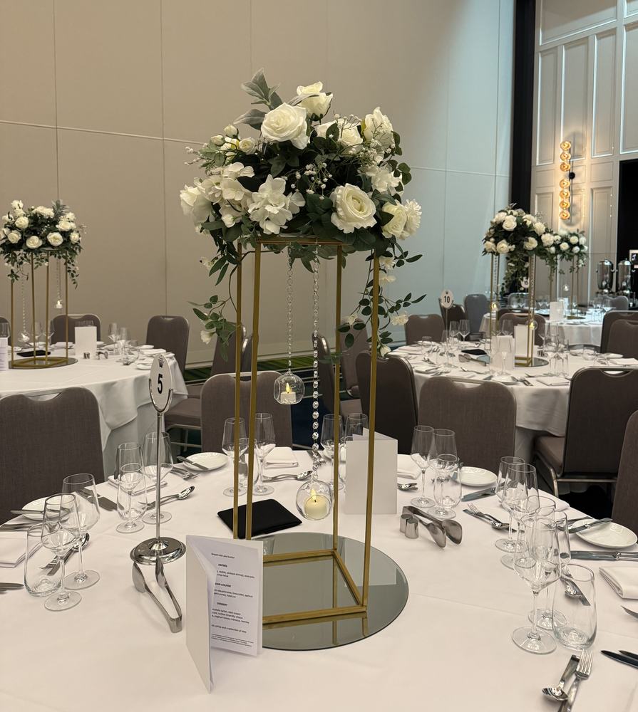 A tall gold stand topped with white flowers on a round guest table